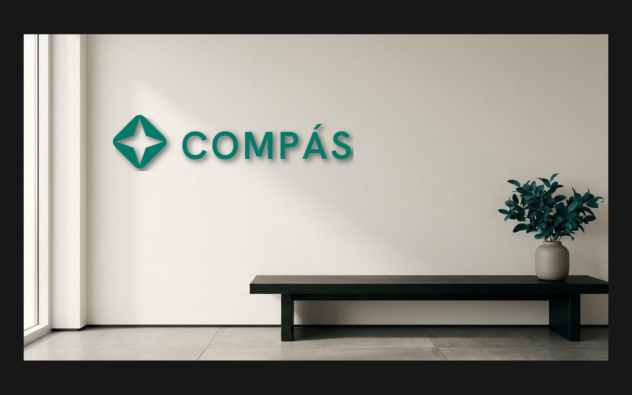 Mockup of the verdigris Compás logo on a white wall above a low bench